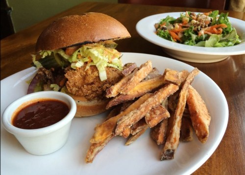 A crispy fried chicken sandwich with lettuce and pickles, served with sweet potato fries and a side salad.