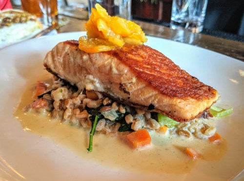 A beautifully plated salmon fillet on a bed of vegetables and grains, topped with citrus slices and a creamy sauce.