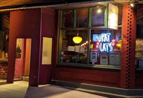 A brightly lit restaurant window with a neon sign reading "Fat Cats" and an inviting open sign.