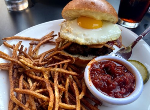 A juicy burger topped with a fried egg, served with crispy fries and a side of dipping sauce.