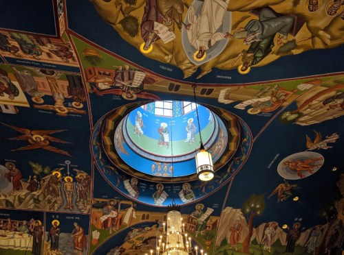 A colorful ceiling mural featuring religious figures and scenes, with a circular skylight in the center.