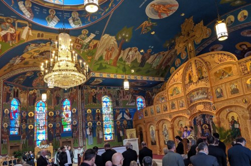 Interior of a beautifully decorated church with vibrant murals, stained glass windows, and a chandelier, during a ceremony.