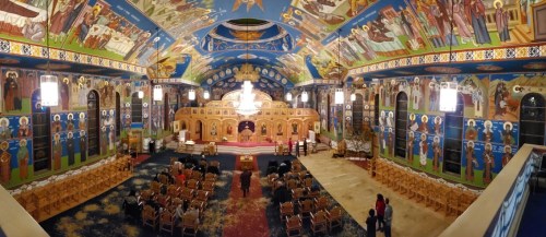 A panoramic view of a beautifully decorated church interior with vibrant murals and a gathering of people.