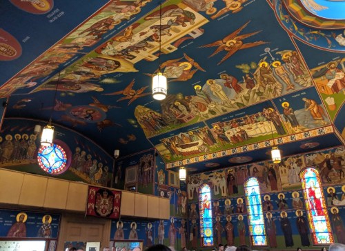 Interior of a church featuring vibrant ceiling murals and stained glass windows depicting religious scenes.