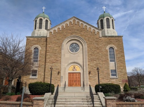 A stone church with a round window and two green domes, featuring a wooden door and decorative landscaping.
