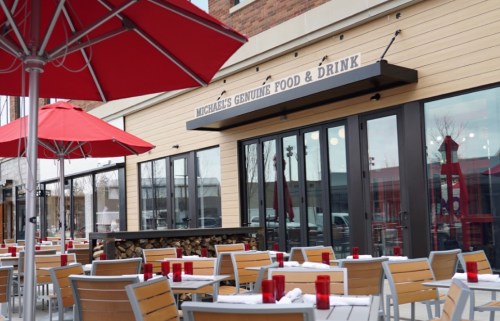 Outdoor dining area with red umbrellas and tables in front of a restaurant named "Michael's Genuine Food & Drink."