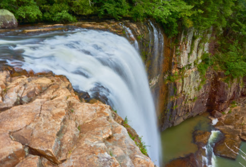 A cascading waterfall flows over rocky cliffs into a serene pool, surrounded by lush green foliage.