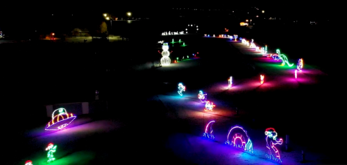 Aerial view of a colorful holiday light display featuring various illuminated figures in a dark park setting.