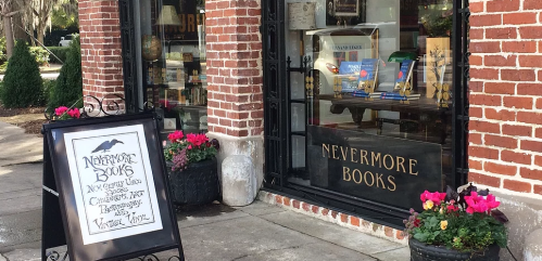 A quaint bookstore named "Nevermore Books" with a sign and colorful flowers outside its brick facade.