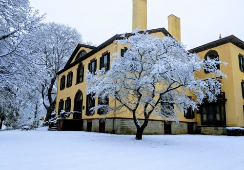 A snow-covered house with large windows, surrounded by frosted trees and a white landscape.