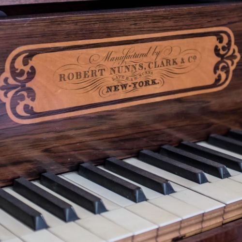 Close-up of a vintage piano's nameplate, reading "Manufactured by Robert Nunns, Clark & Co, New York."