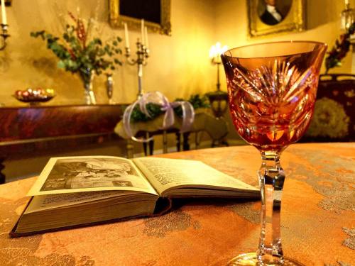 A close-up of a crystal glass beside an open book, with a softly lit, elegant room in the background.