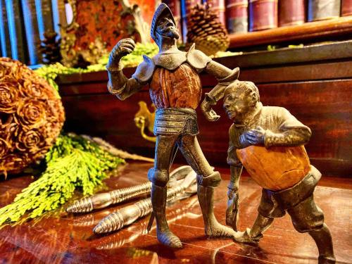 Two vintage figurines, one in armor and the other in a tunic, posed on a wooden surface with decorative elements in the background.