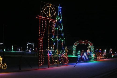 Colorful holiday lights illuminate a winter scene, featuring a large tree and festive decorations against a dark night sky.