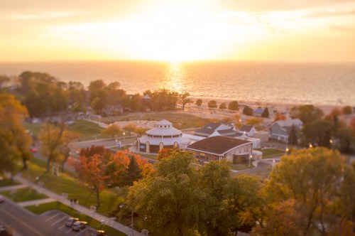 A sunset over a lake, with trees and a park in the foreground, and a building near the water's edge.