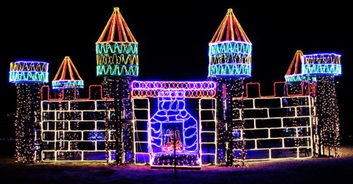 A brightly lit castle made of colorful holiday lights, featuring towers with pointed roofs against a dark night sky.