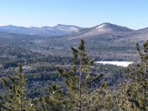 A scenic view of mountains and forests under a clear blue sky, with a hint of snow on the peaks.