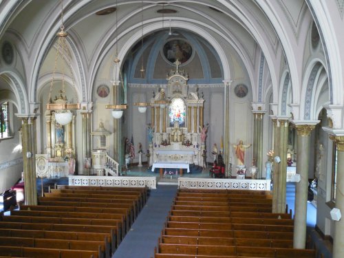 Interior of a church featuring an altar, stained glass, and wooden pews, with ornate architectural details.