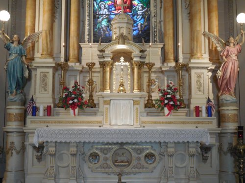 A beautifully decorated altar with statues, flowers, and a stained glass window in a church setting.