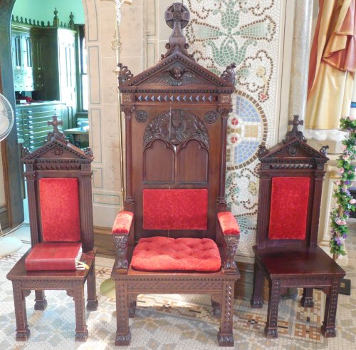 A set of ornate wooden chairs with red upholstery, featuring intricate carvings and a tall central throne.