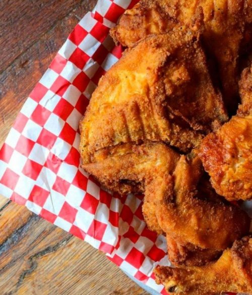 A close-up of crispy fried chicken pieces on a red and white checkered paper.