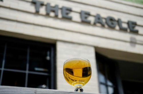 A glass of golden beer sits on a ledge in front of a building with the sign "The Eagle."