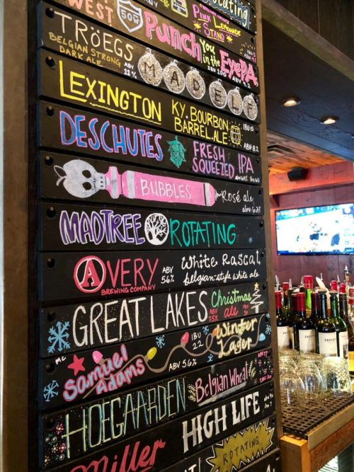 A colorful chalkboard menu displaying various craft beers and their details at a bar.