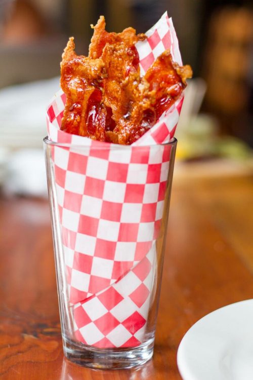 A glass filled with crispy fried bacon strips wrapped in red and white checkered paper.
