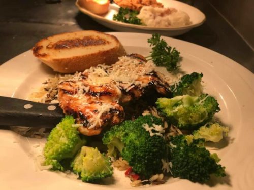 Grilled chicken with broccoli, rice, and a slice of toasted bread, garnished with parsley and cheese.