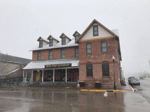 Historic brick building with a snow-covered roof, featuring a restaurant sign, in a snowy landscape.