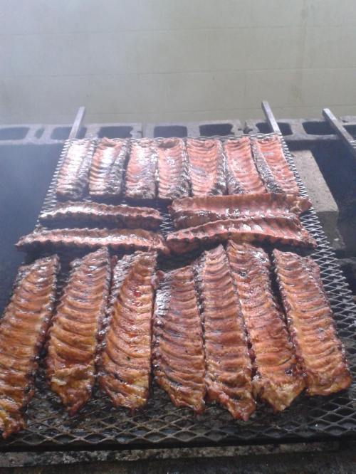Grilled ribs cooking on a barbecue grill, with a smoky background and a shiny, caramelized surface.