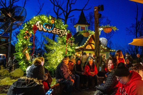 A festive scene with a decorated arch, people sitting, and holiday lights glowing in a twilight setting.