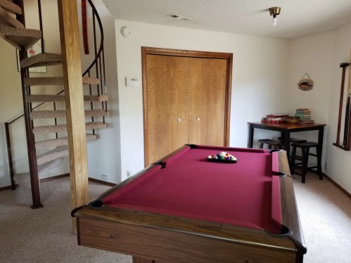 A room featuring a pool table with balls, a spiral staircase, and a wooden table with books against a wall.