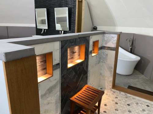 Modern bathroom featuring a freestanding tub, illuminated wall niches, and a wooden stool. Elegant tile and decor.