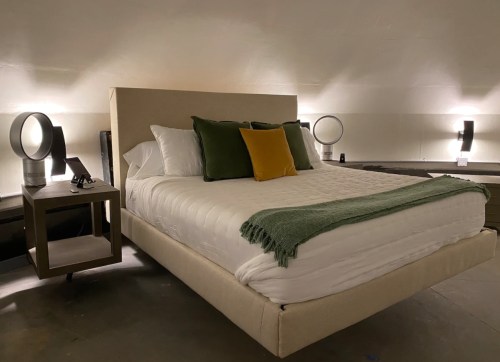 A modern bedroom featuring a bed with white linens, green and yellow pillows, and stylish bedside lamps.