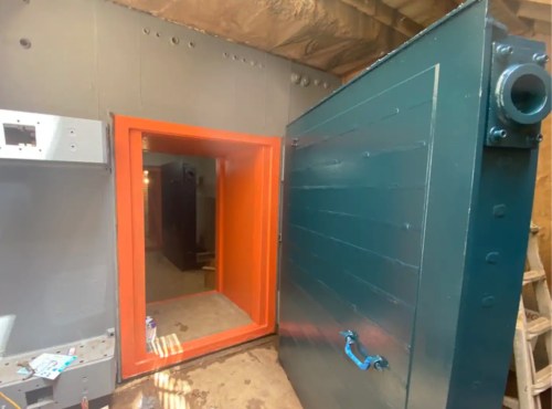 A large, industrial door with an orange frame opens into a spacious, unfinished room with exposed walls and flooring.