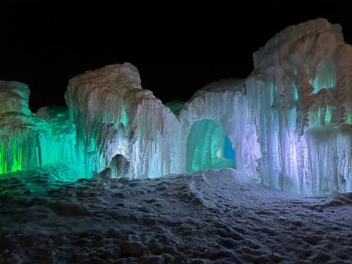 Colorful ice formations illuminated in green and blue, creating a magical winter landscape at night.