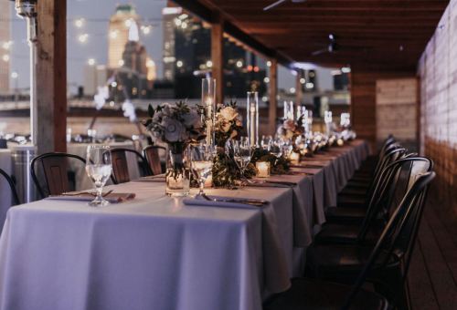 A beautifully set dining table with candles and flowers, overlooking a city skyline at night.