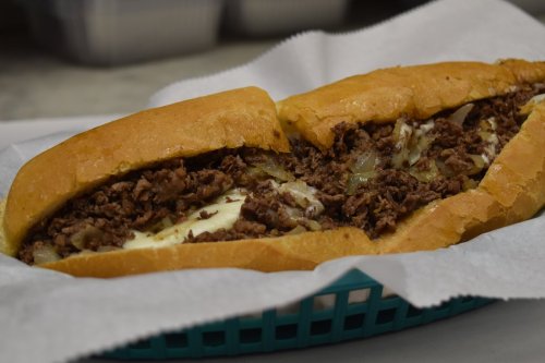 A close-up of a cheesesteak sandwich with chopped beef and melted cheese in a toasted hoagie roll, served in a basket.