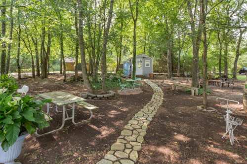 A serene outdoor space with a stone path, picnic tables, and a small shed surrounded by trees.