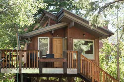 A cozy wooden cabin on stilts surrounded by trees, featuring a deck and large windows.