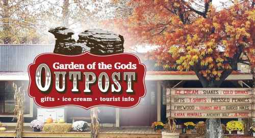 Sign for Garden of the Gods Outpost, featuring gifts, ice cream, and tourist information, surrounded by autumn trees.