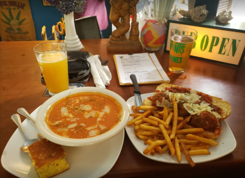 A bowl of soup with bread, a plate of meatballs and fries, a glass of orange drink, and a beer on a wooden table.