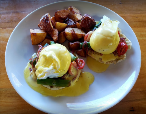 A plate of eggs Benedict with poached eggs, tomatoes, and asparagus, served with roasted potatoes.
