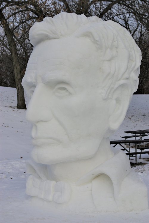 A large snow sculpture of a man's head, resembling Abraham Lincoln, set against a snowy landscape.