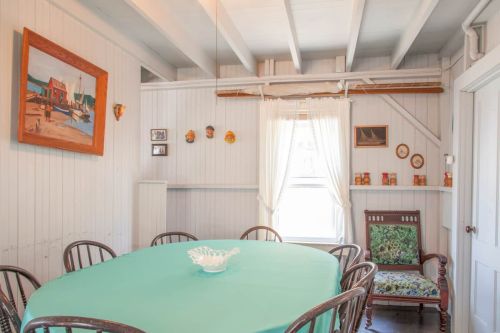 A cozy dining room with a round table, wooden chairs, and nautical-themed decor on the walls.