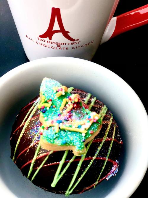 A chocolate dessert topped with a colorful cookie and sprinkles, next to a mug that says "Eat Dessert First."