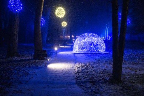 A snowy path illuminated by blue lights, featuring a glowing igloo structure and decorative orbs in the trees.
