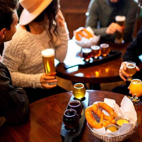 A group of friends enjoying drinks and pretzels at a cozy table in a bar.