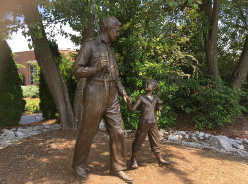 A bronze statue of a man and a boy holding fishing rods, walking together in a garden setting.